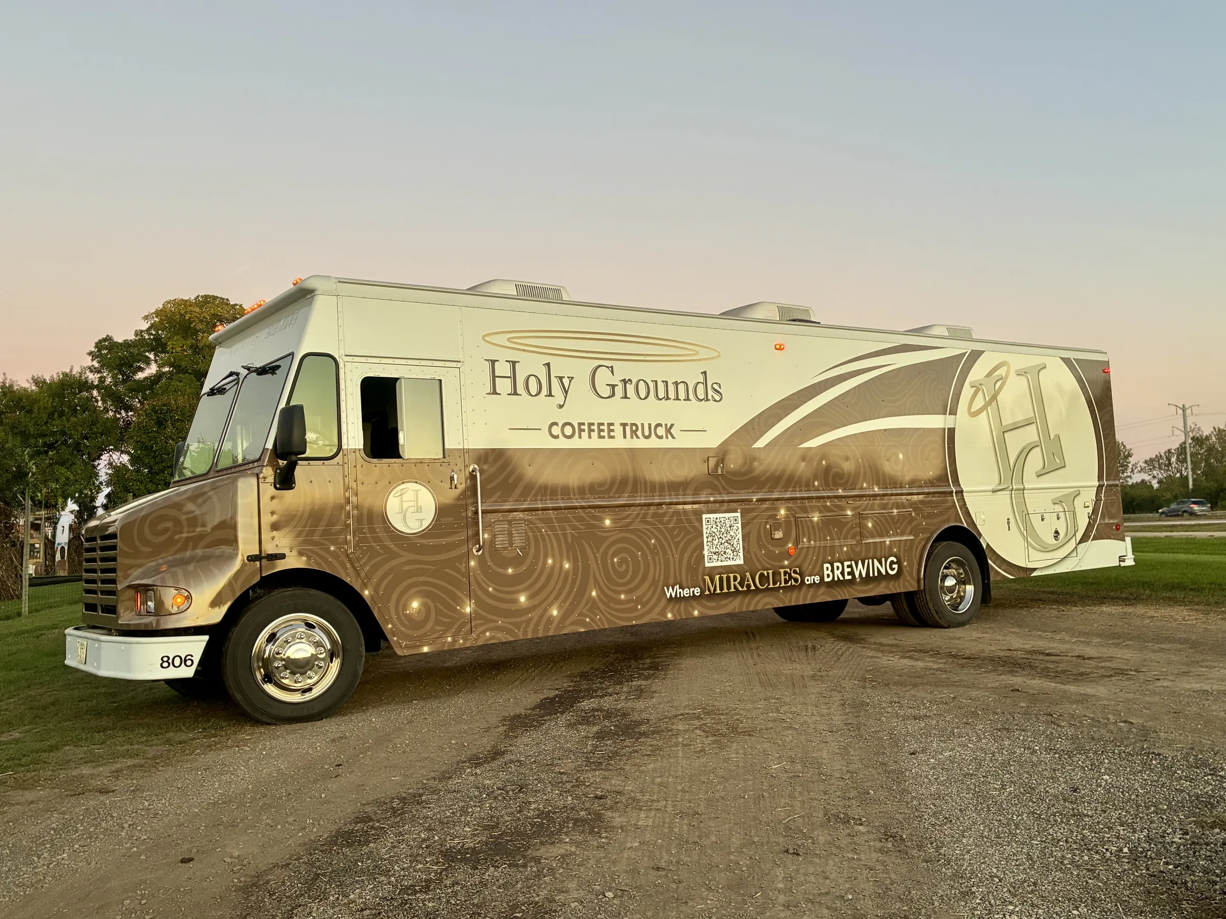 The brown and cream Holy Grounds Coffee Truck parked outdoors at sunset